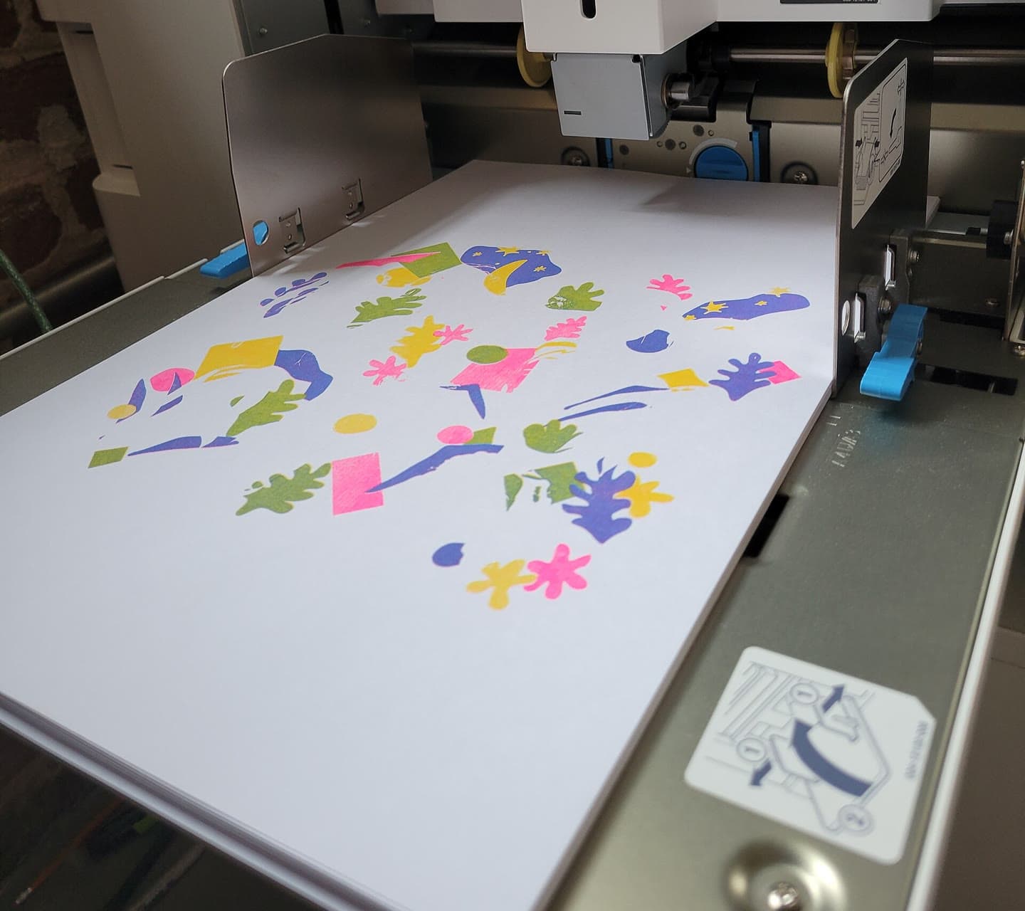 A freshly printed sheet with pink, yellow, blue and green shapes on the delivery tray of a risograph duplicator